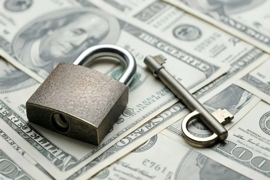 Padlock and key on dollar bills symbolizing financial protection tenants need after rental application approval.