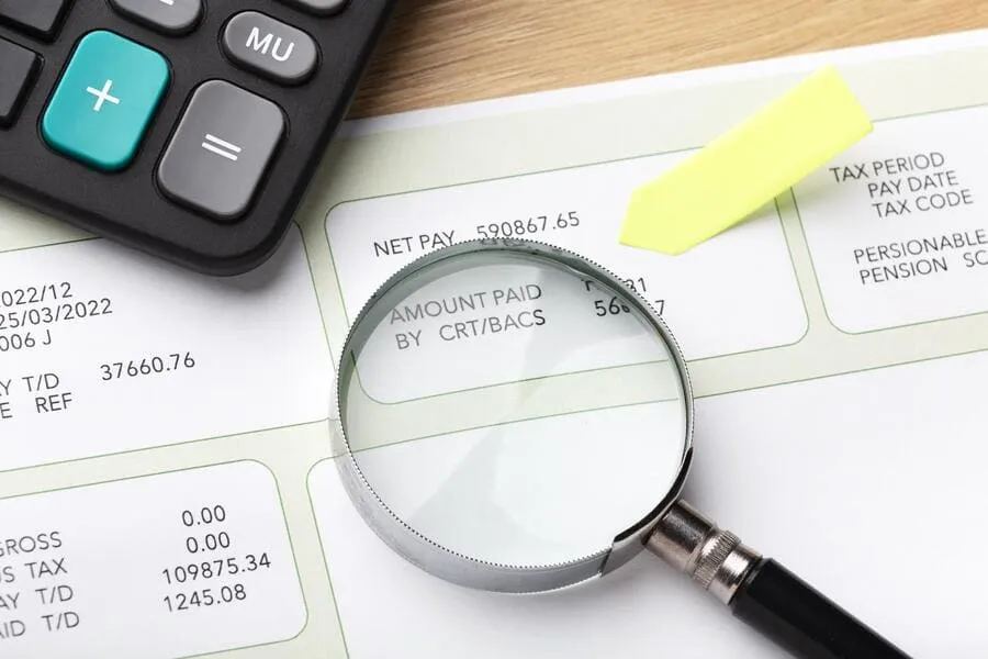 Magnifying glass over a payslip showing net pay, the income verification step behind an RS3 score.