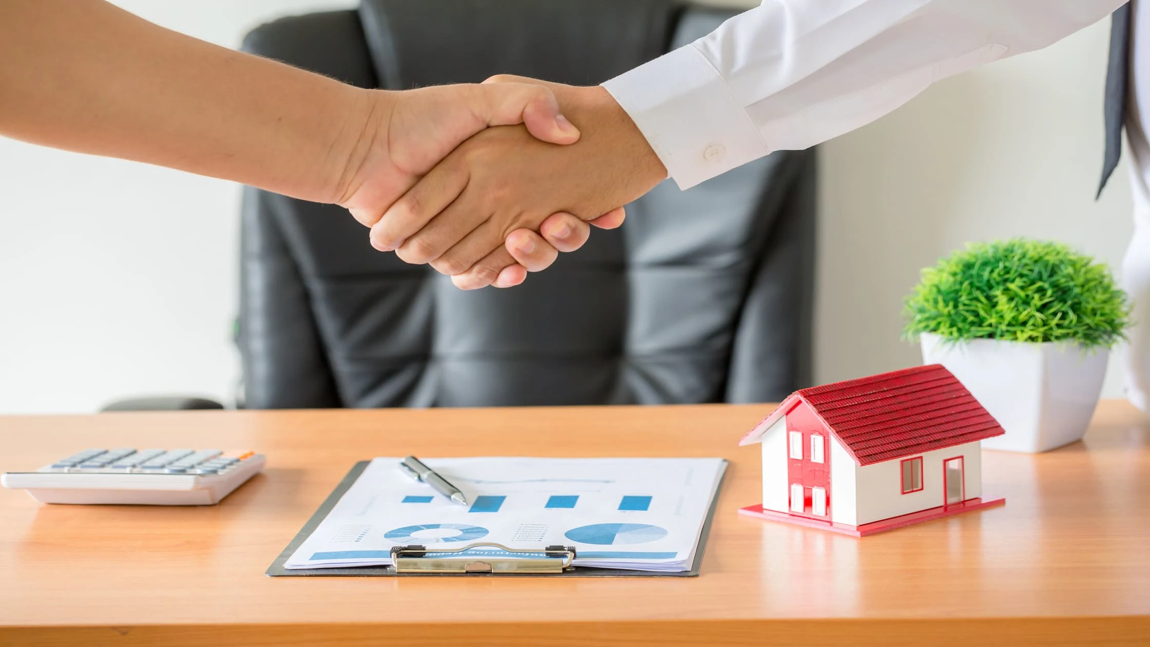 landlord-and-tenant-handshake-over-lease-agreement-deal-with-house-model-on-desk