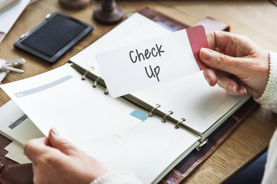 Hand pulling a Check Up tab from a personal planner binder on a wooden desk